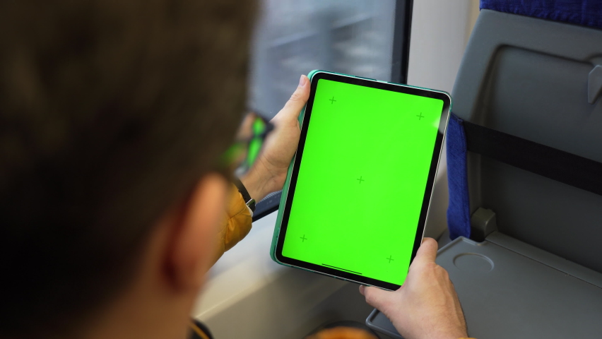 Back view of man watch tablet pc with green screen and browsing online in train. Mock up for watching content on pad. Blank digital phone in hand of guy sitting indoors in public transport | Shutterstock HD Video #1088182121