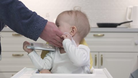 Father wiping face of his one-year-old son with baby wipes after feeding him in the kitchen. High quality 4k footage