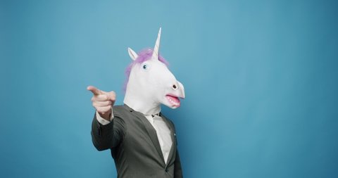 Funny Guy in Gray Suits Dance with Unicorn Mask, he is having fun on isolated Blue Background, Having Fun, Party Halloween. Slow Motion. April 1, Fool's Day. Masquarade idea. Good, and sign Like.