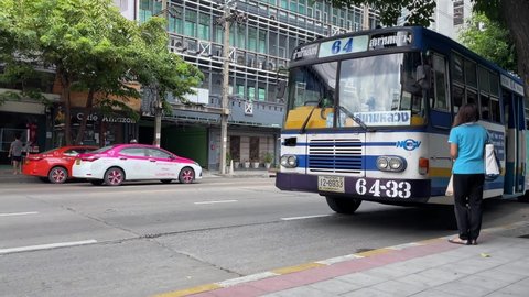 BANGKOK, THAILAND - Circa November, 2021: People get on and off the bus at bus stop during daytime with building and cafe on the other side of the road. Bus number 64 goes on route to Sanam Luang