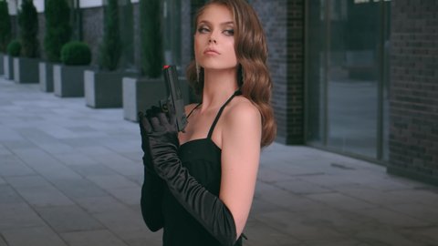 Carnival clothes costume sexy fantasy woman killer holding gun hand in long glove. Strong girl fashion face. dangerous successful sexy lady. Black elegant evening dress. Backdrop building modern city