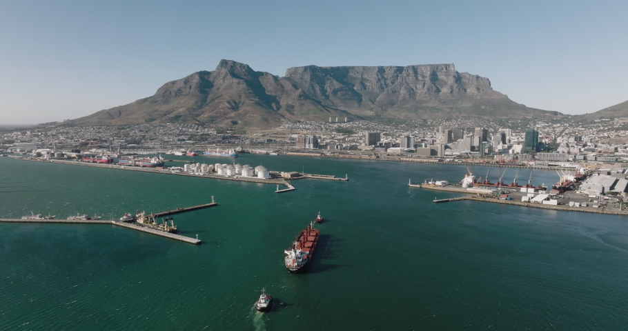 Spectacular aerial view of a container ship being pulled by tug boats entering Cape Town Harbour, Table Mountain and City Centre in the background,Cape Town, South Africa. Global supply chain
