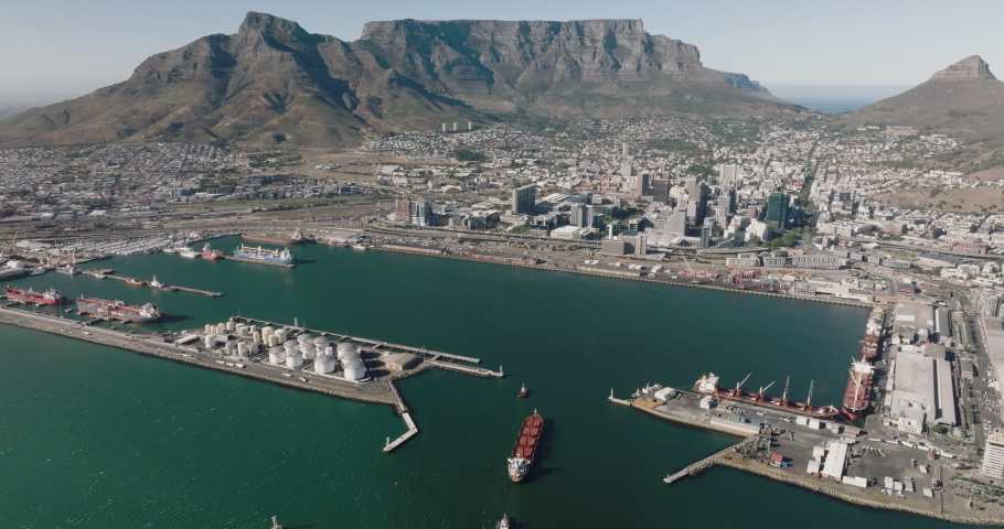 Spectacular high aerial view of a container ship being pulled by tug boats entering Cape Town Harbour, Table Mountain and City Centre in the background,Cape Town, South Africa. Global supply chain
