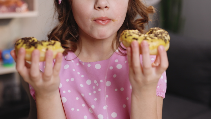 Close up of unrecognizable kid brunette girl mouth eating vegan doughnut with chocolate banana icing. Woman face is eating two donuts at the same time. Sweet addiction concept