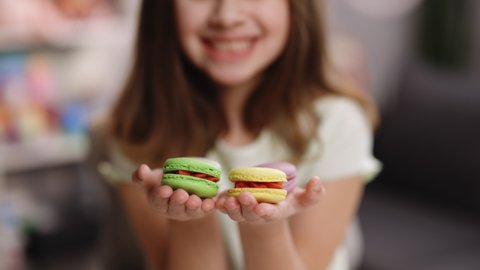 Teen girl plays with dessert macarons. Close up macro view of fresh green and yellow macaroon dessert in hands of woman sitting at home