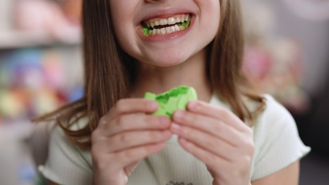 Close up of gorgeous school girl biting french macaroon, enjoying eating, confectionary desire and pleasure. Attractive brunette female girl on home background, licks her lips, eating macaron