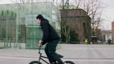 TRACKING Caucasian teenager kid performing tricks while riding his BMX bicycle in the city. Shot with 2x anamorphic lens