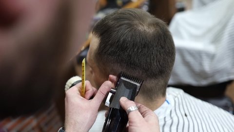 Close-up of hair cutting with a trimmer on the head of a customer with pink hair. The master barber in black gloves carries out a quality haircut in an authentic barbershop. Macro slow motion.