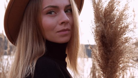 Millennial woman European blonde woman smiling with beige hat in black sweater in the countryside. Golden hour, cottagecore. Local travel. Slow living. Mental health. Pampas grass
