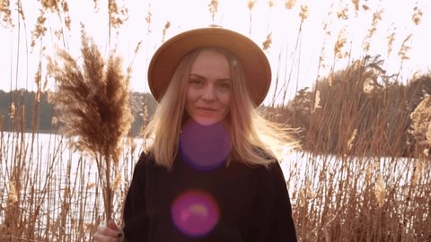 Millennial woman European blonde woman smiling with beige hat in black sweater in the countryside. Golden hour, cottagecore. Local travel. Slow living. Mental health. Pampas grass