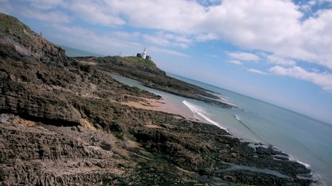 Aerial view of Bracelet Bay the Gower Peninsula South Wales with Mumbles lighthouse, located near to Swansea city, Fpv drone footage of the coast