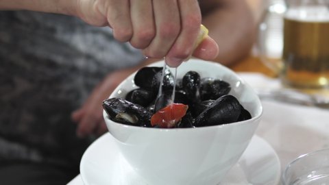 Man putting lemon juice on the freshly cooked mussels in the decorated plate in a resturant
