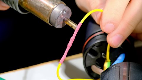 Worker deals with heat-gun for heat shrink tubing on wires for pump plug cable. Professional specialist and equipment at workshop closeup