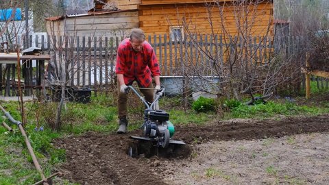 Old man plows the ground with a motor cultivator. A farmer ploughs the soil using a petrol cultivator. 