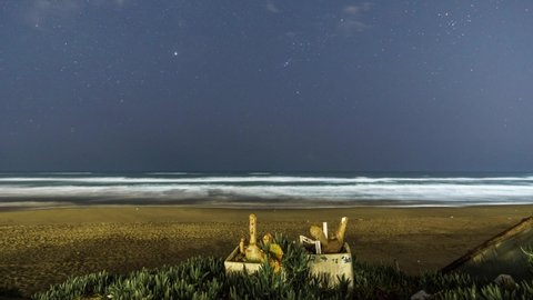Stars at night with constellation of orion moving over beach at mediterranean sea, Italy
