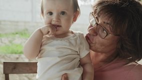 Video of a grandmother holding her niece in her hand, playing and having fun together. Family day. Baby care.