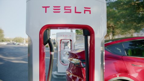 Los Angeles, California USA, March 2022. Luxury EV vehicles charging battery. Red SUV Tesla autonomous electric cars refilling energy at free of charge super fast charging station on parking lot 6K