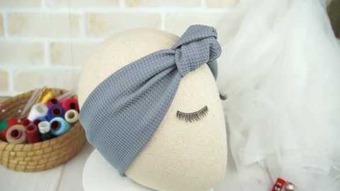 A mannequin wearing headband with knot pattern made out of knit fabric in dark gray color, great as hair accessories for babies and kids.