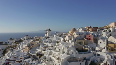 Aerial: Slow panning drone shot of Oia in Santorini, Greece during golden hour