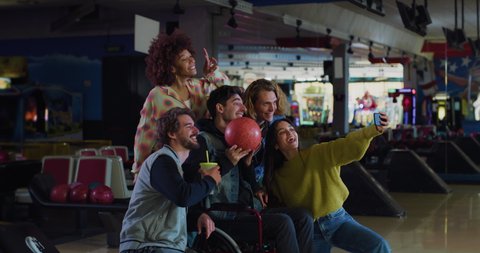 Cinematic shot of happy young multiracial college friends are having fun to make selfie together with smart phone while play bowling on weekend in sporting club.