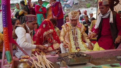 A Happy Indian bride and groom or a married couple dressed in ethnic attire are performing a ritual during a Hindu wedding ceremony in the countryside and rural area, Manali, India (March 2022)