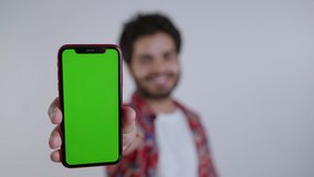 Young Indian Asian Smiling male extending hand showing Green Screen or Chroma key on a Smartphone. A male or trendy stylish guy with a new mobile phone app or a brand isolated on white background.  - Powered by Shutterstock - Get 15% off with code: PIKWIZARD15