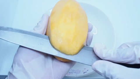 Footage full HD 1080P, person wearing white gloves, peeling ripe mango, on a white plate, Thai fruit that is popular to eat in summer.