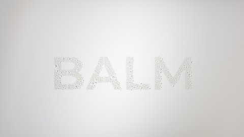 Writing balm printed on the wet glass blown off with air stream on grey background | balm commercial concept