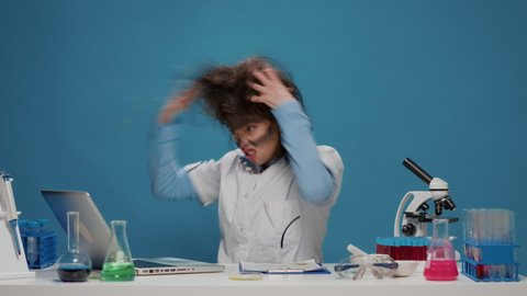 Amusing crazy scientist working on laptop and acting insane, doing goofy silly facial expressions and pulling her hair. Funny foolish specialist feeling confused and desperate on camera.