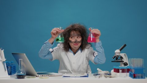 Crazy amusing scientist analyzing substance in beakers on camera, having wacky hair and dirty face after explosion. Mad insane woman acting goofy and foolish, being silly and messy.
