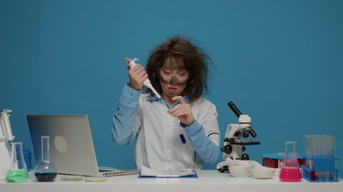 Insane goofy scientist using micro pipette and test tube in front of camera, acting crazy in studio and doing foolish silly facial expressions. Amusing funny female chemist with dirty face.
