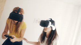 Exited girls in VR helmets at home. Two women in virtual reality headsets sitting on bed, playing video games and having fun together. 3D technology. concept of virtual reality, Gaming, friendship.