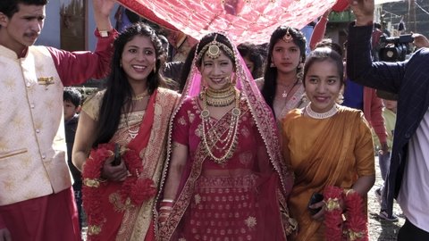 Indian Hilly Marriage at village Jhalpari, Pauri Garhwal, Uttarakhand, India - February 2 2022: Indian girl in traditional wedding dress Lehanga Choli on her marriage day with bridesmaids.