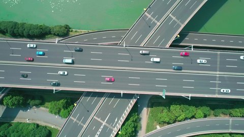 Aerial top down view with camera rotation of a highway overpass multilevel junction with fast moving cars surrounded by green trees and with a river on a side on a sunny day.