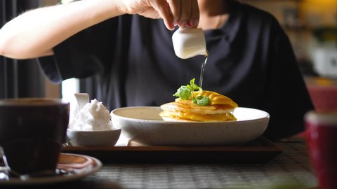 Female pours maple syrup on delicious pancakes. Young woman eating breakfast in vegan restaurant. High quality healthy food 4K footage.