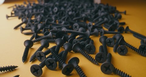 Hand picking black screws that fall out of the box. Super macro close up black screws slow motion view  on an orange background.
