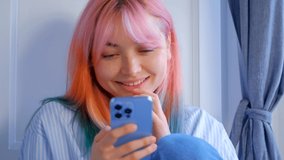 Happy Ukrainian girl browsing internet on mobile phone and laughing. Cute white female with dyed rainbow hair using modern smartphone with cheerful smile