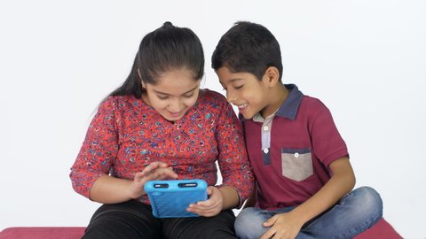 Sibling rivalry - Indian brother and sister fighting for a digital tablet. Indian siblings sitting against the white background and using a tablet - technology concept.
