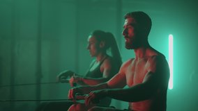 Muscular man and sporty woman workout on training simulator in crossfit gym. Muscular sporty man and women workout on training simulator in gym. Sportswomen exercising on rowing machines - Powered by Shutterstock - Get 15% off with code: PIKWIZARD15