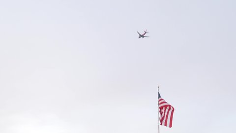 Plane flying in sky, american flag waving in wind, California USA. Airplane or aircraft departured from airport. Travel, tourism or vacations concept. Star-spangled banner symbol of united states.