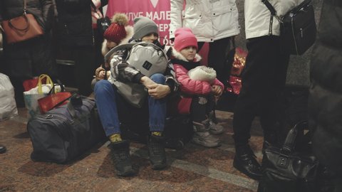 Lviv, Ukraine - March 15, 2022: Little children sitting at the floor. Refugees at the railway station waiting train after leaving their home. Forced migration and flight of people from battlefields