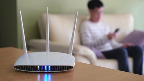 Selective focus at router. Internet router with people hand type Wifi password on his smartphone to login. Fast and high speed internet connection from fiber line with LAN cable connection.