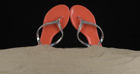 Pair of pink flip flops embellished with rhinestones stick out of the sand. Panorama. Isolated on black background