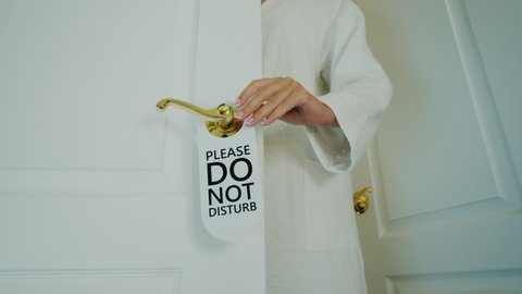 Woman in bathrobe hangs Do Not Disturb sign on doorknob of door