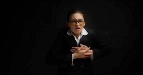 A business lady with glasses suffers from chest pain at work. A beautiful Asian woman in office clothes has a heartache, a heart attack, myocarditis, she has fever, pressure. On a black background