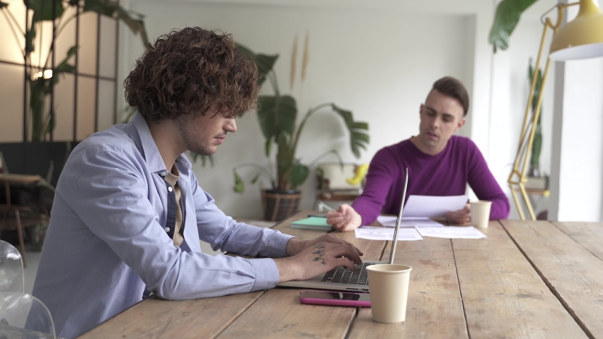 Young gay couple reading good news in document, smiling excited by mail letter, checking paying domestic bills online on laptop, discussing budget planning 