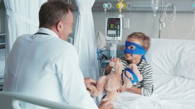 Cute little boy with superhero mask embracing teddy bear while playing with doctor. Playful child dressed as superhero holding stuff toy talking to pediatrician. Doctor visiting his little patient. - Powered by Shutterstock - Get 15% off with code: PIKWIZARD15
