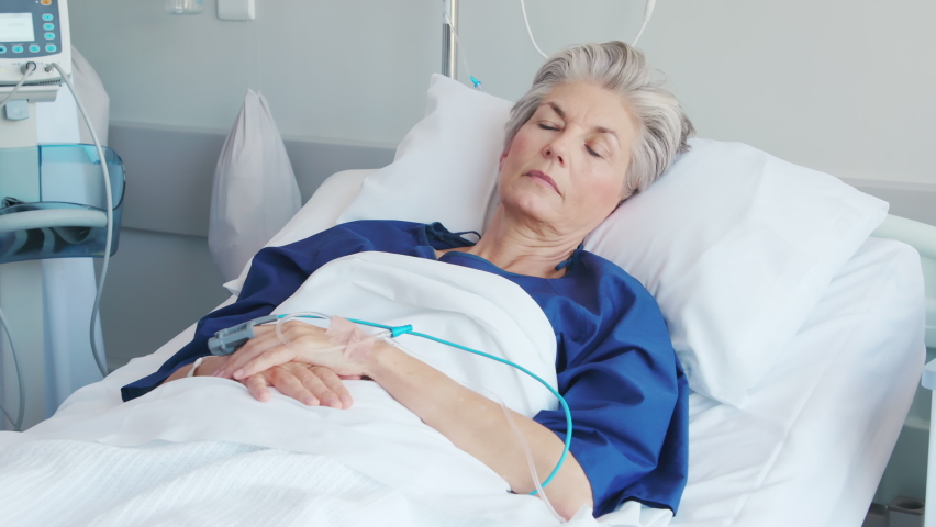 Mature woman recovering from illness while lying on hospital bed. Portrait of old hospitalized patient recovering after surgery. Happy senior woman in hospital ward while looking at camera. Royalty-Free Stock Footage #1088219757