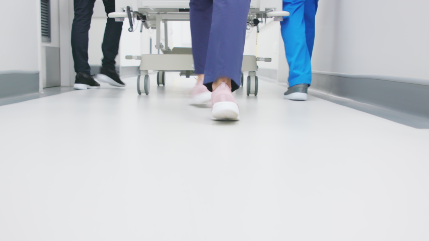 Close up of doctor and nurses feet rushing stretcher in emergency ward at hospital. Medical stuff pushing gurney in hospital. Detail of feet of medical team running in hurry to operation theatre. Royalty-Free Stock Footage #1088219763