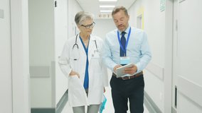 Senior woman doctor having a discussion in hospital hallway with medical staff. Pharmaceutical representative showing medical report on digital tablet about new medicine or therapy. - Powered by Shutterstock - Get 15% off with code: PIKWIZARD15
